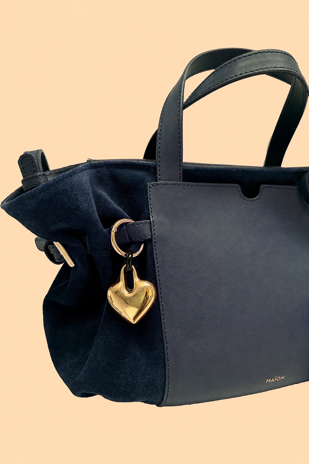 Charm cœur en métal doré Maïon, accroché à un sac en cuir velours bleu