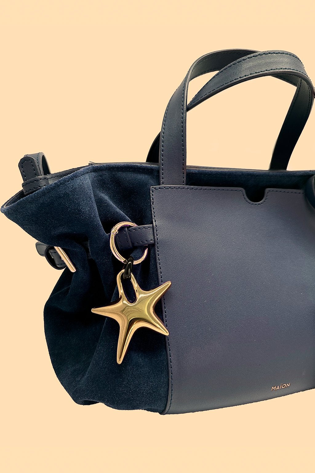 Charm étoile en métal doré Maïon, accroché à un sac en cuir velours bleu