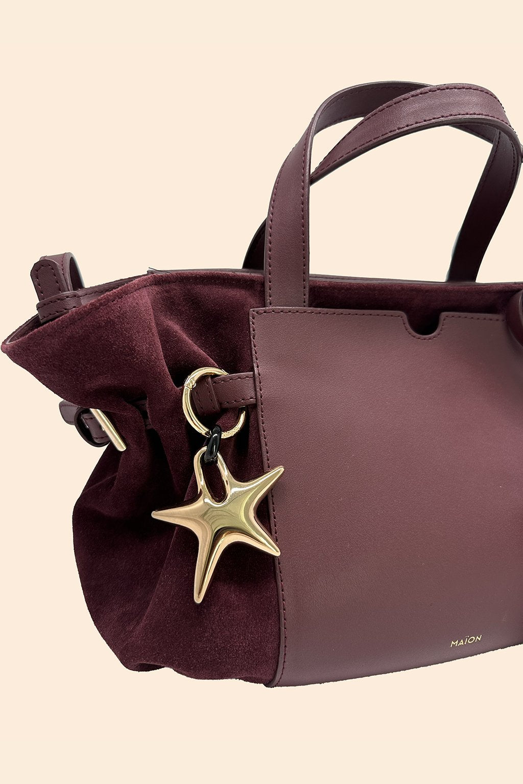 Charm étoile en métal doré Maïon, accroché à un sac en cuir velours bordeaux