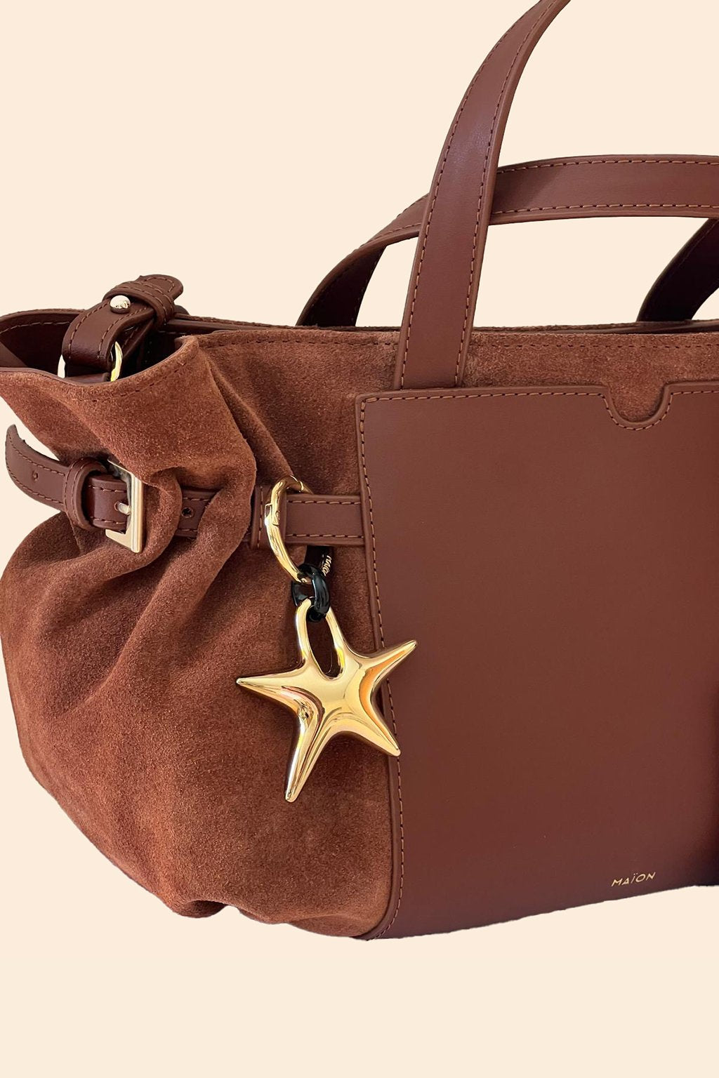 Charm étoile en métal doré Maïon, accroché à un sac en cuir velours marron